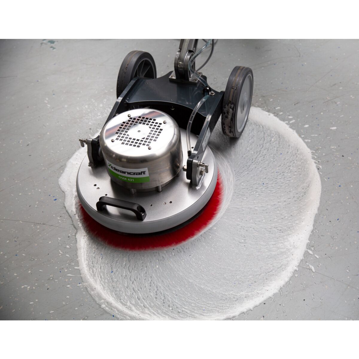 Bodenreinigungsmaschine mit roter Bürste verteilt Reinigungsschaum auf grauem Industrieboden.