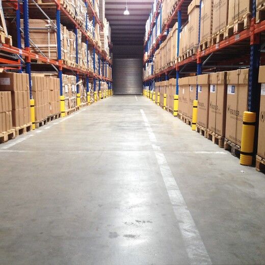 Gelbe Kunststoff-Anfahrschutze an Regalstützen in Lagerhalle schützen vor Kollisionen im breiten Gang mit Kartons.