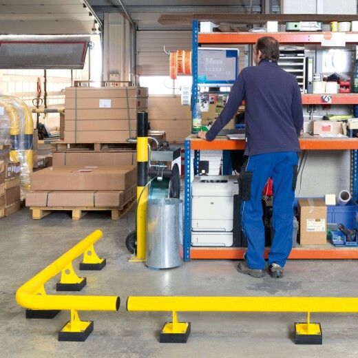 Gelbe Sicherheitsbarriere trennt den Computerarbeitsplatz eines Mitarbeiters im Lager deutlich vom restlichen Arbeitsbereich.