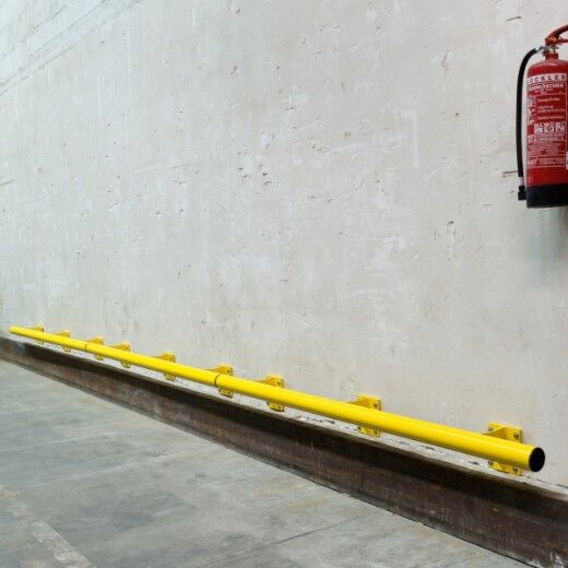 Gelbe Schutzbarriere entlang einer Wand in einer Industriehalle, schützt vor Anfahrschäden; Feuerlöscher an der Wand montiert.