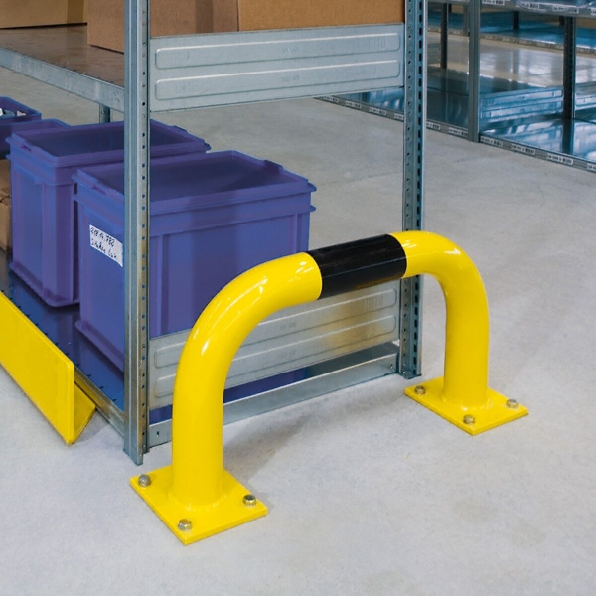 Foto: Niedriger gelber Schutzbügel mit schwarzem Streifen vor einem Metallregal mit blauen Kunststoffboxen in Lagerhalle.