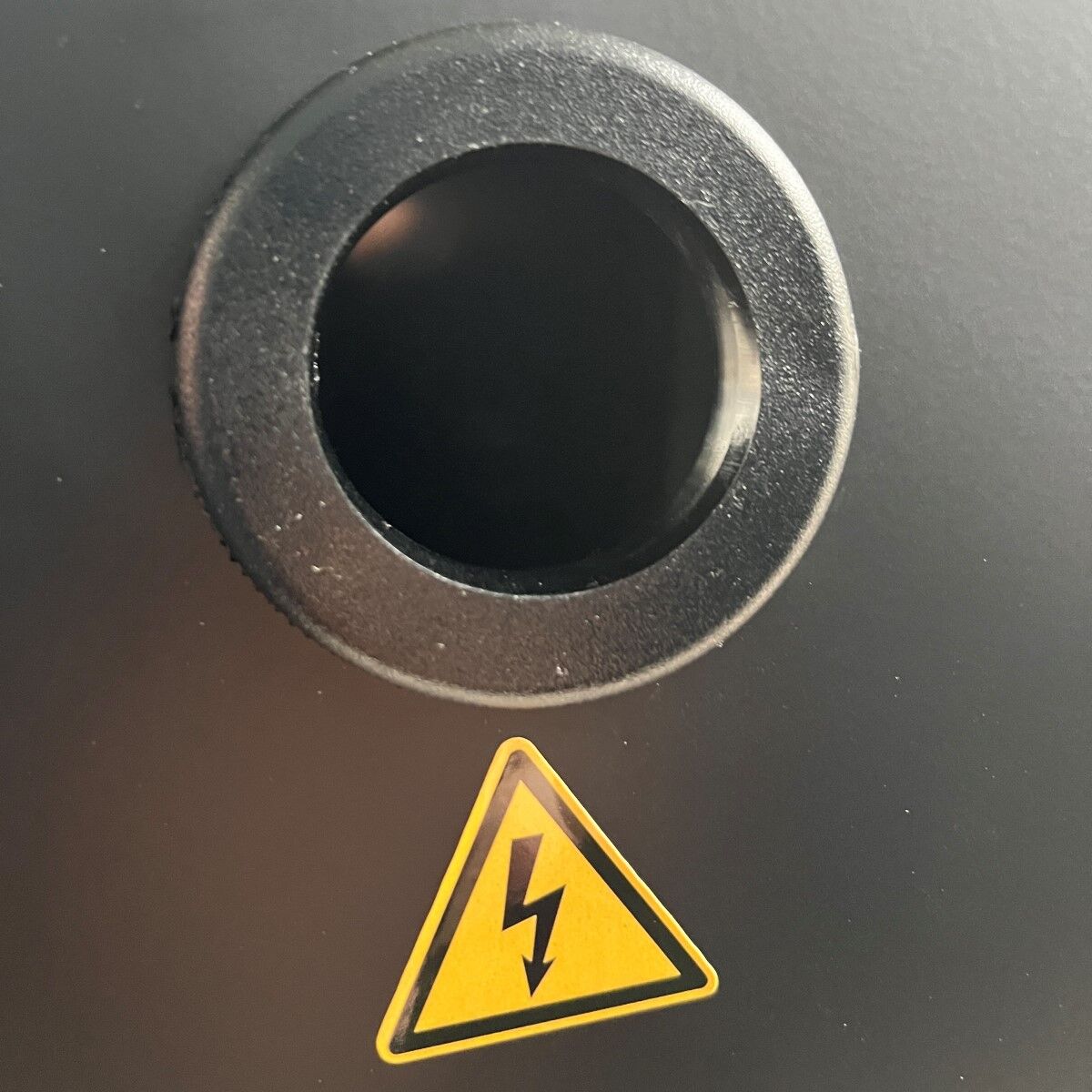 Schwarze Geräteöffnung mit gelbem Warnsymbol für elektrische Spannung darunter.