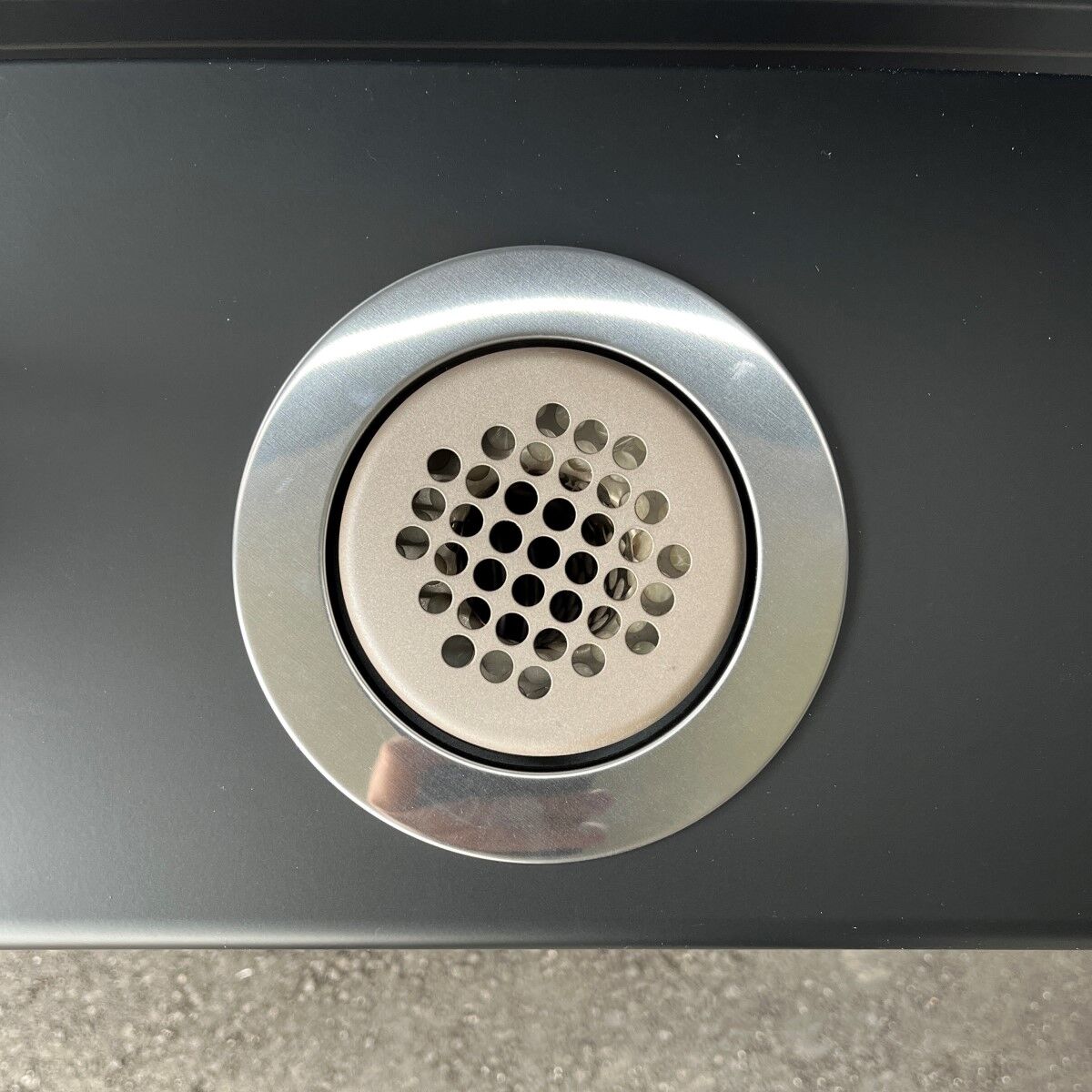 Runde Metallbelüftung mit gelochter Abdeckung in einer schwarzen Geräteoberfläche.