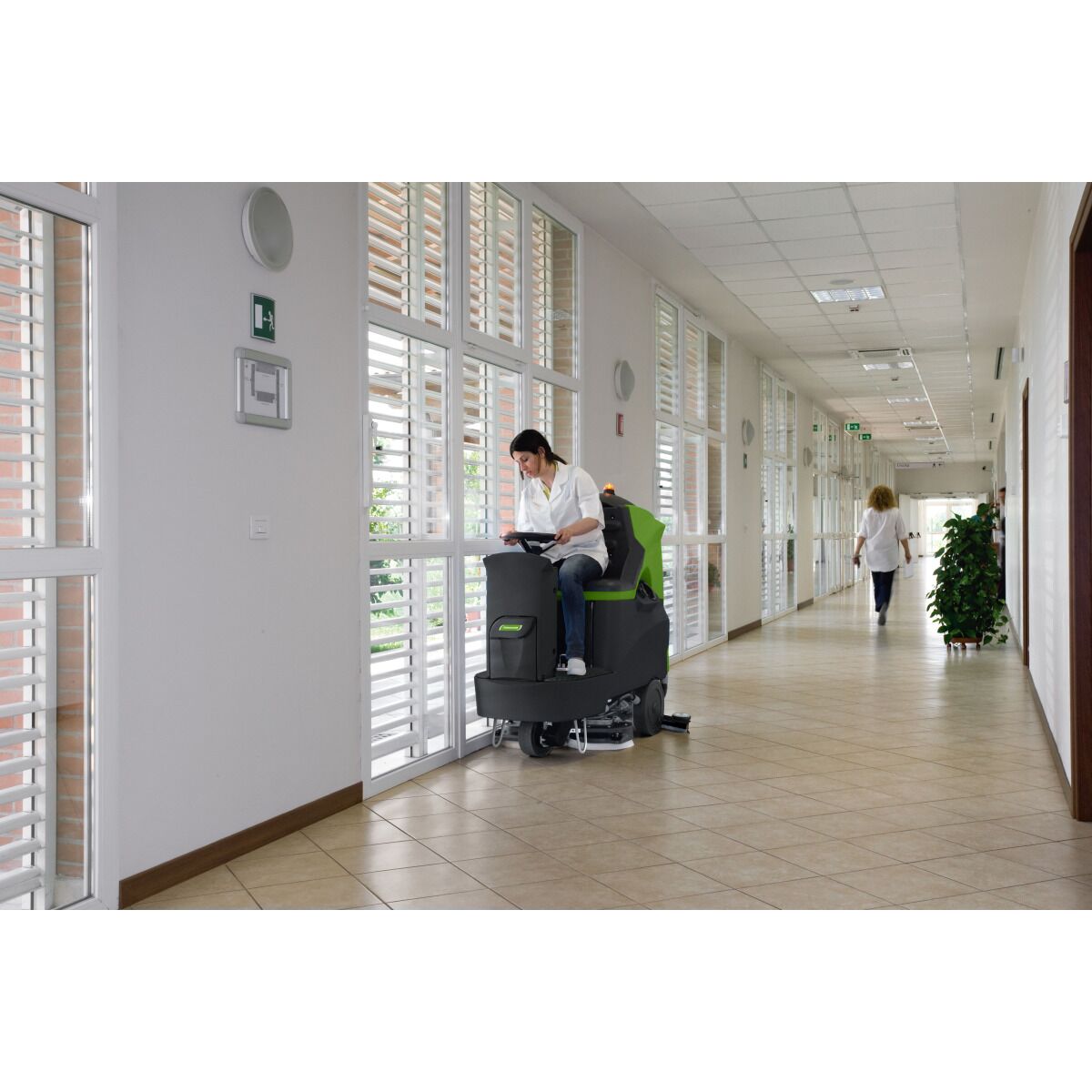 Aufsitz-Scheuersaugmaschine wird in einem hellen Gebäudeflur von einer Person gefahren.