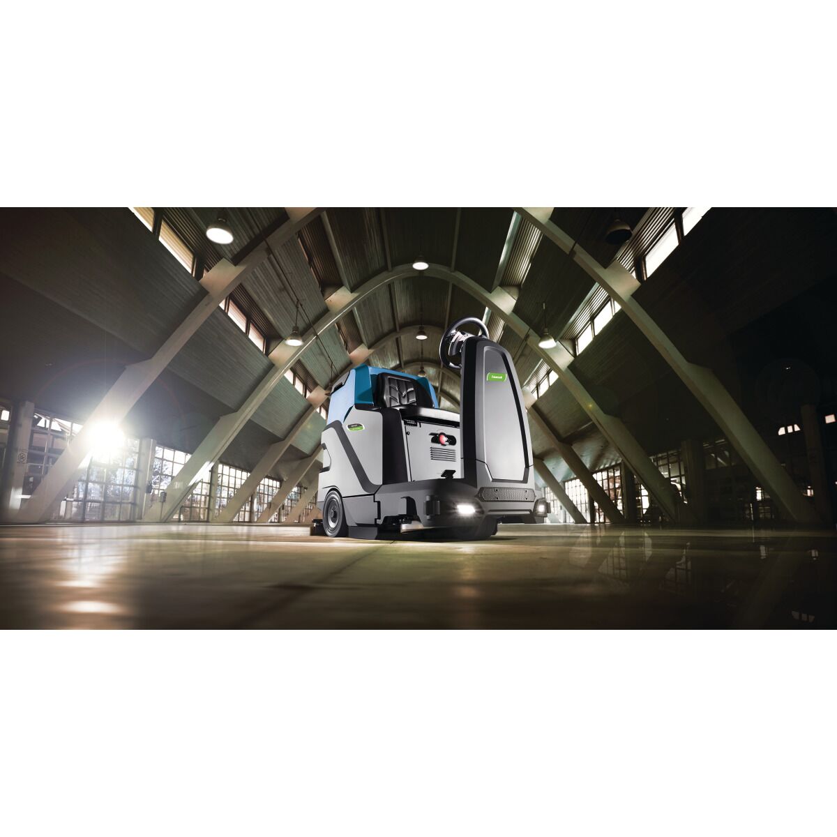 Eine Aufsitz-Scheuersaugmaschine reinigt den Boden einer großen Halle mit gewölbtem Dach.