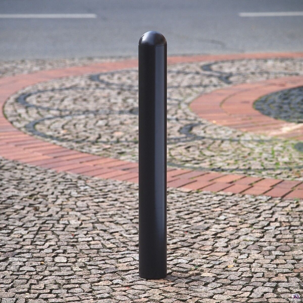 Schwarzer Poller auf Kopfsteinpflaster; im Hintergrund Straße und Gehwegmuster.