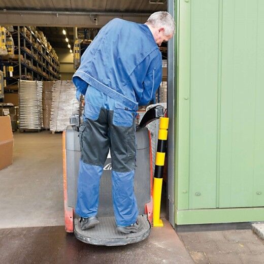 Mitarbeiter mit Hubwagen fährt gegen gelben, flexiblen Rammschutz-Poller an einer Lagerhalleneinfahrt – schützt Tür und Fahrzeug.