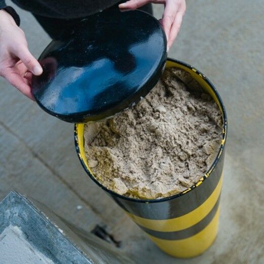 Geöffneter gelb-schwarzer Poller, gefüllt mit Sand, Deckel wird von einer Person abgenommen.