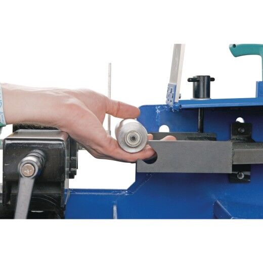 Hand legt Rundrohr in Halterung der Bandschleifmaschine ein.