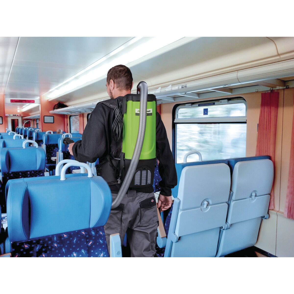 Reinigung eines Zugabteils mit grünem Rucksackstaubsauger, getragen auf dem Rücken.