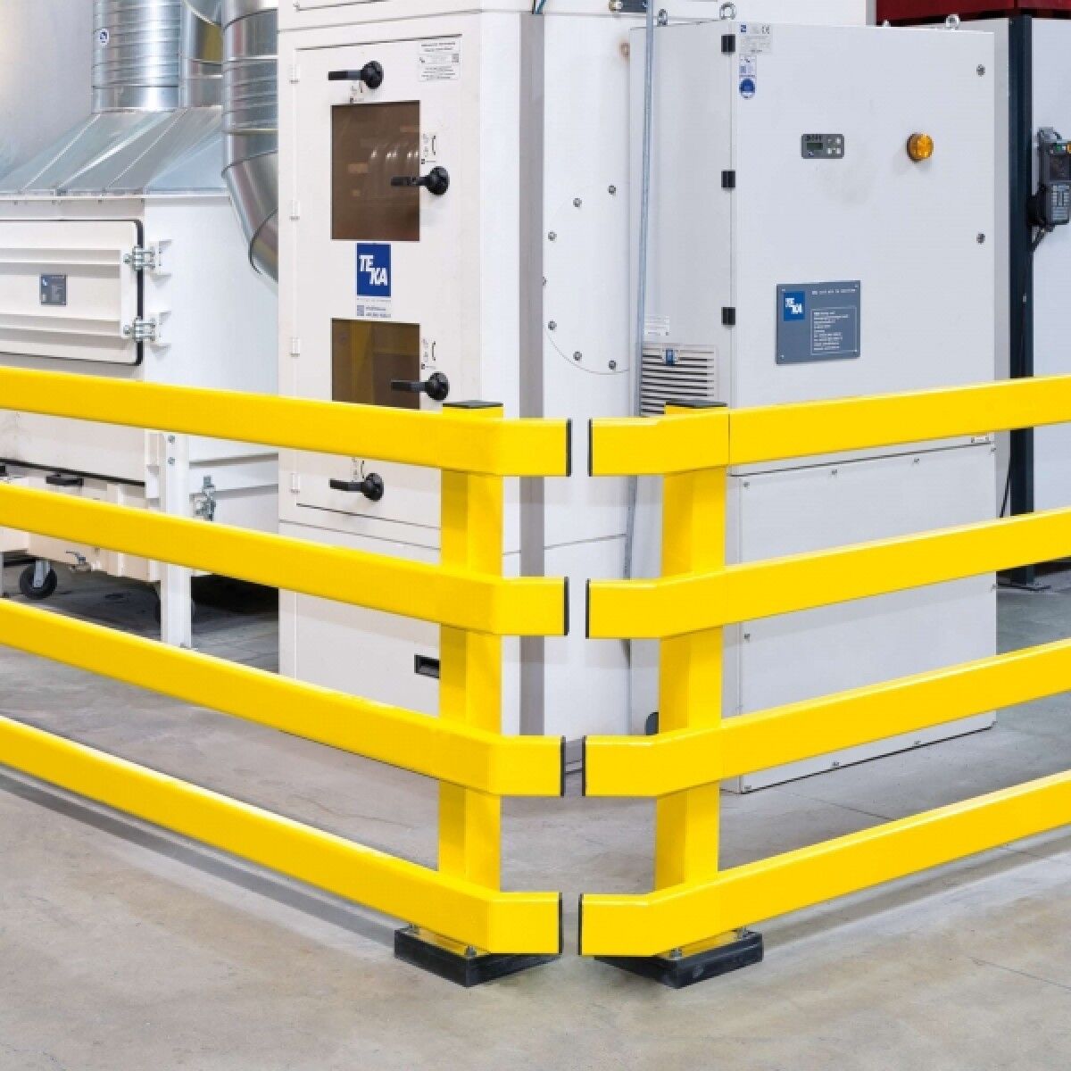 Gelbes vierreihiges Rammschutzgeländer als Ecke um weiße Industrieanlage; schwarze Sockel an den Pfosten.