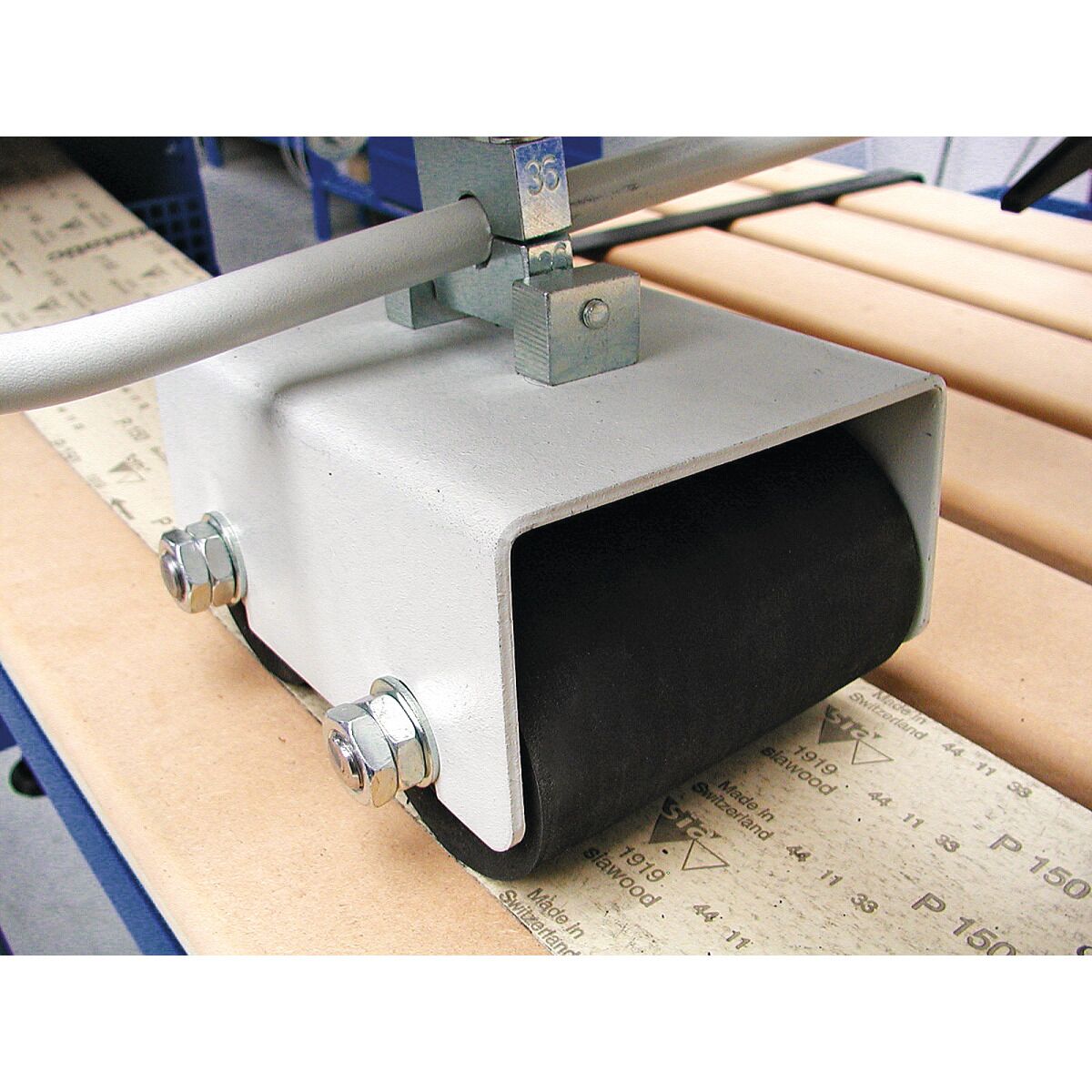 Nahaufnahme einer Andruckrolle auf dem Schleifband über der Holzauflage der Langbandschleifmaschine.