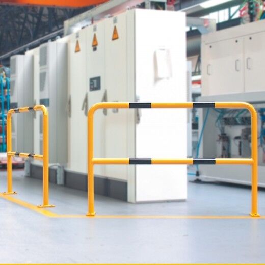 Gelbe Schutzbarriere mit schwarzer Markierung trennt Maschinenbereich von Gehweg in heller Industriehalle mit Schaltschrank.