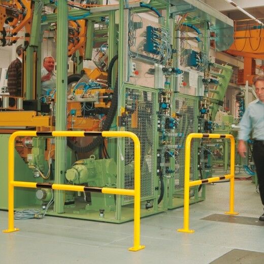 Gelbe Schutzbarriere sichert Maschinenbereich in Produktionshalle, ein Mann geht rechts daran vorbei.