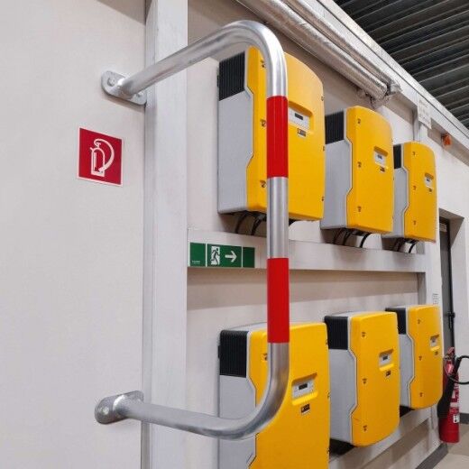 Langer U-förmiger Metallbügel mit roten Streifen als Rammschutz vor gelben Geräten an einer Wand in einem Technikraum montiert.