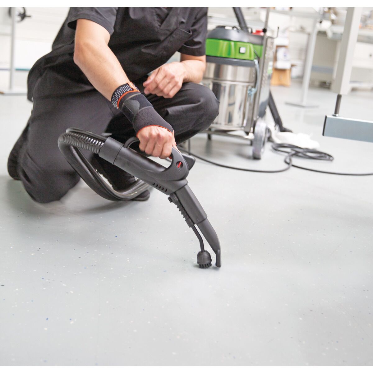 Person in Arbeitskleidung verwendet einen Dampfreiniger mit Bürstendüse zur Bodenreinigung.