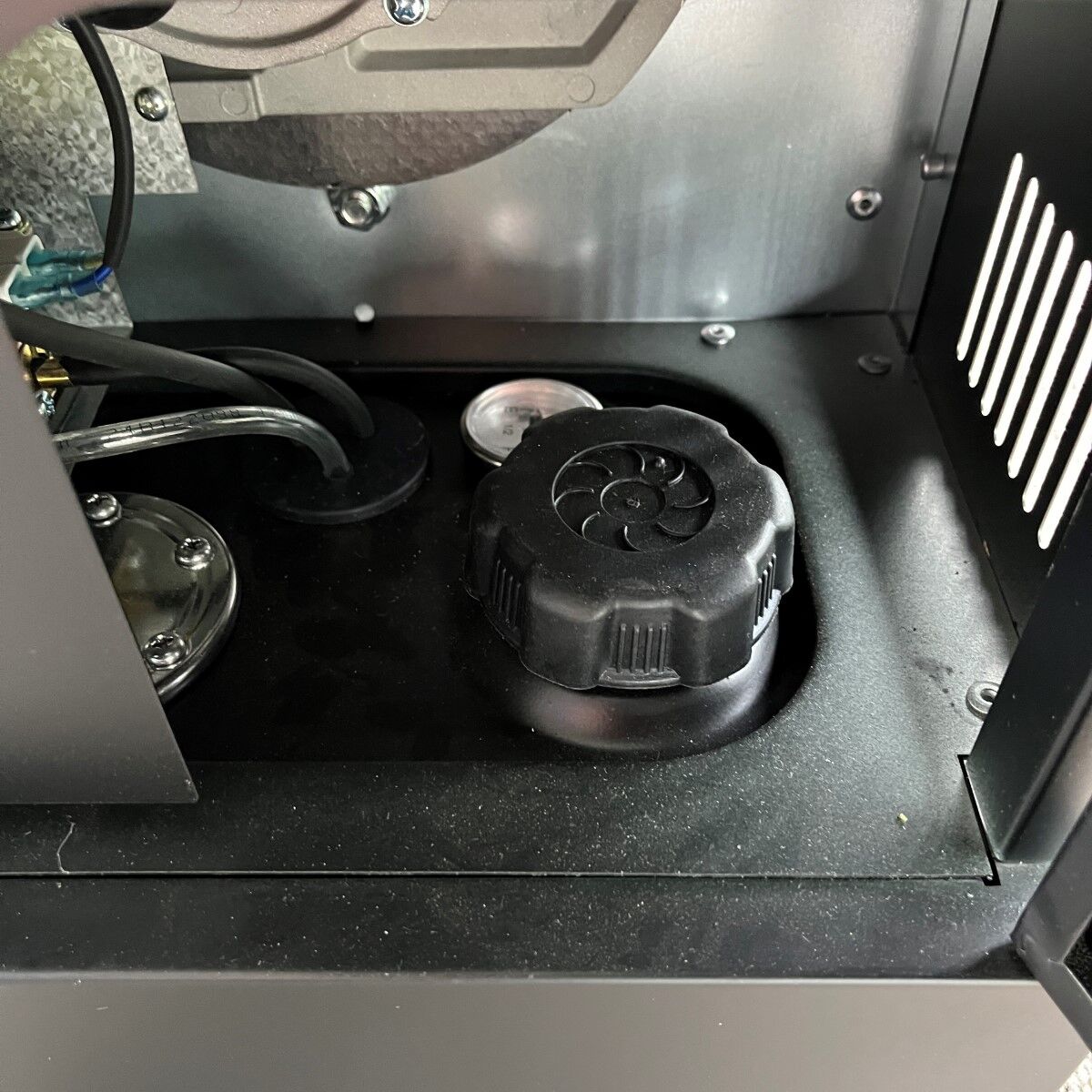 Nahaufnahme eines schwarzen Kunststoffverschlusses mit Kabeln und Metallteilen in einem Geräteinneren.