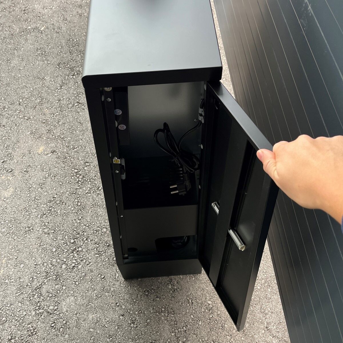 Geöffnetes Seitenfach eines schwarzen Heizgeräts mit sichtbarem Innenraum und Kabeln.