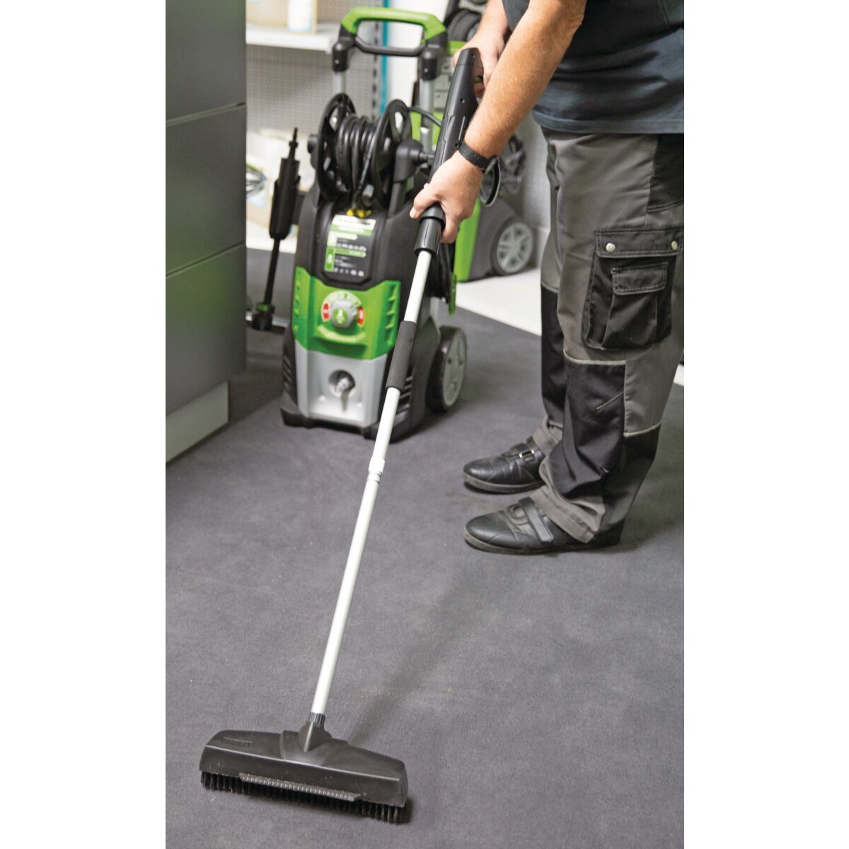 Anwendungsbild: Person reinigt mit Hochdruckreiniger und Bodenaufsatz eine Oberfläche im Innenbereich.