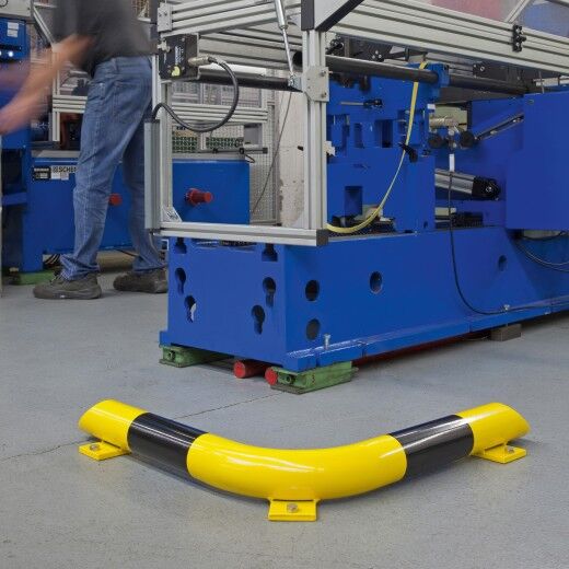 Gelb-schwarze Schutzbarriere in C-Form vor einer Maschine, dient als Aufprallschutz im industriellen Arbeitsbereich.